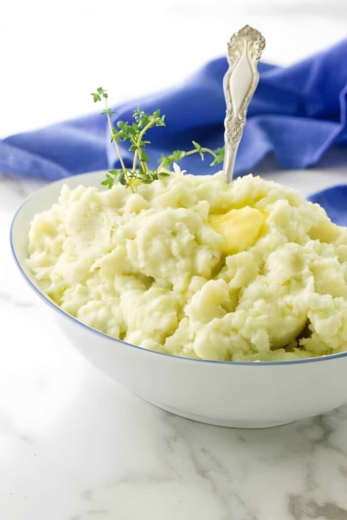 Bowl of ricotta mashed potatoes with butter, herbs, and silver spoon.