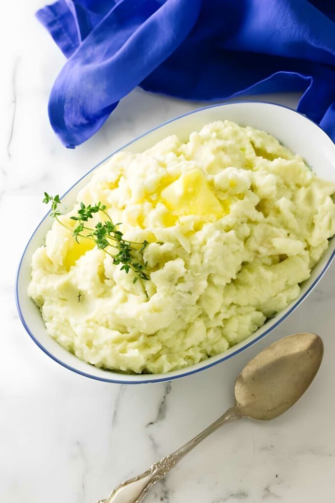 Ricotta mashed potatoes with butter and thyme in white dish.