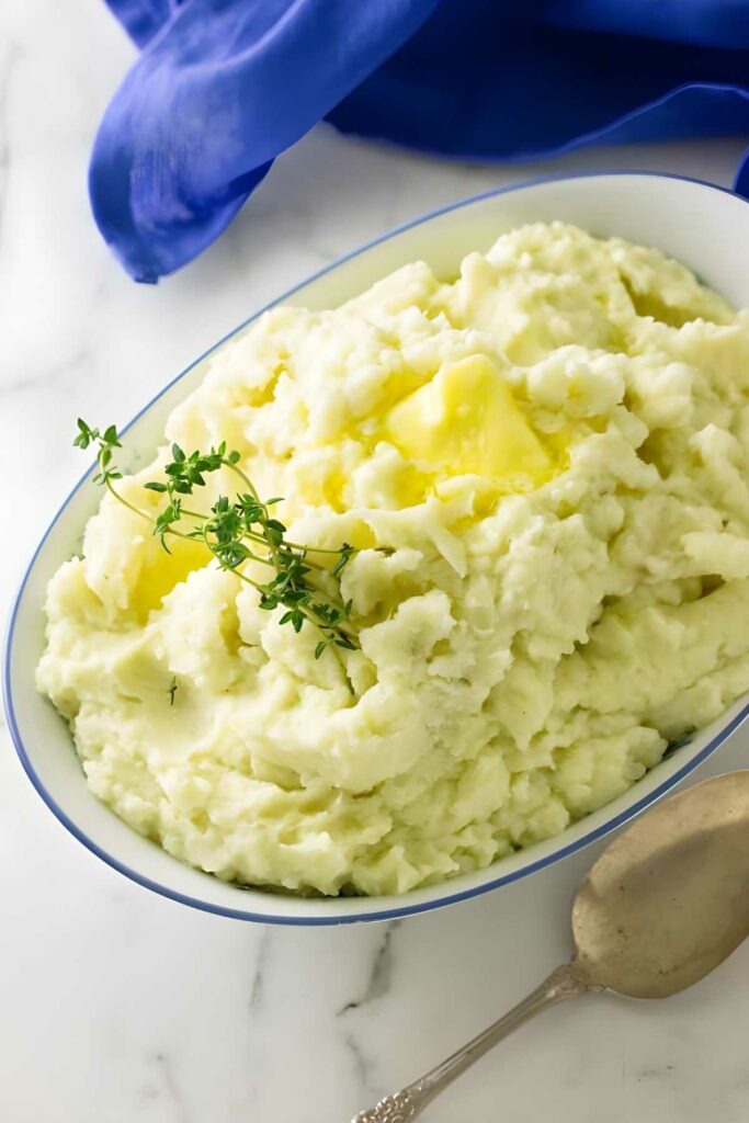 Mashed potatoes with butter and thyme in dish on marble surface.