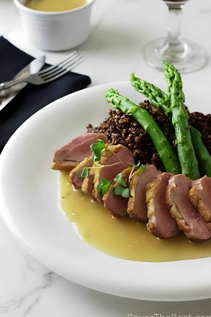 Roasted Duck Breast with Ginger-Rum Sauce Sliced duck breast with sauce, quinoa, and asparagus on white plate.