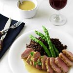 Sliced duck breast with quinoa, asparagus, and wine on an elegant table.