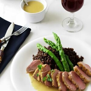 Sliced duck breast with quinoa, asparagus, and wine on an elegant table.
