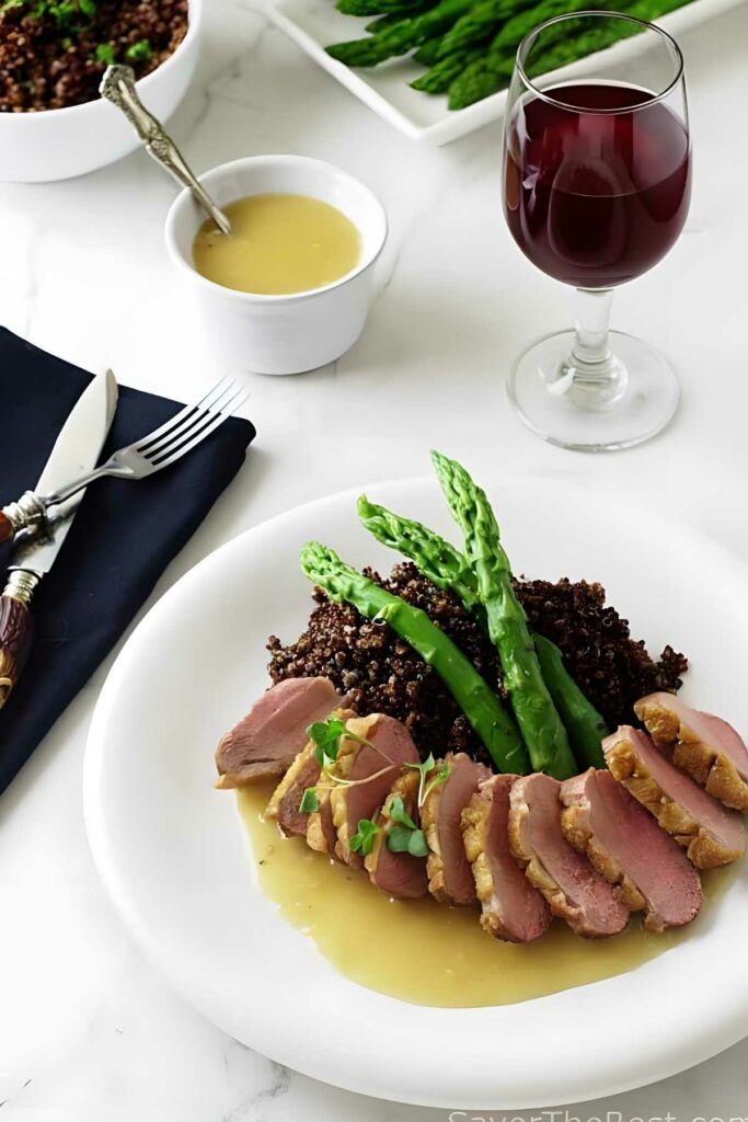 Roasted Duck Breast with Ginger-Rum Sauce Sliced duck breast with quinoa, asparagus, and wine on an elegant table.