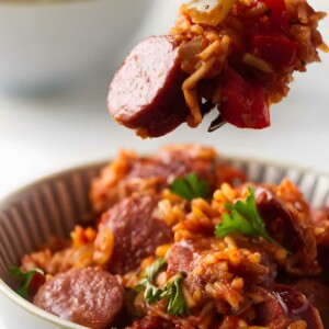 Fork holds sausage, rice, and peppers above bowl of jambalaya.