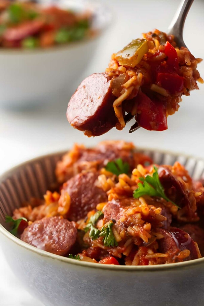 Fork holds sausage, rice, and peppers above bowl.