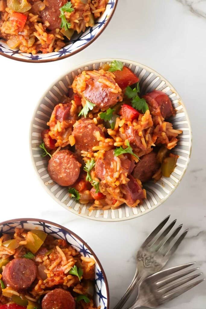 Bowl of jambalaya with sausage and vegetables, surrounded by smaller bowls.