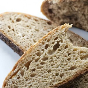 Two slices of rustic sourdough bread with airy crumb, loaf behind.
