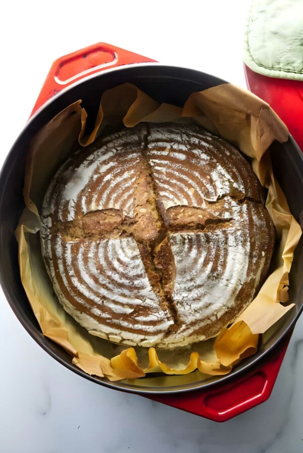 Round artisan spelt bread in red Dutch oven.