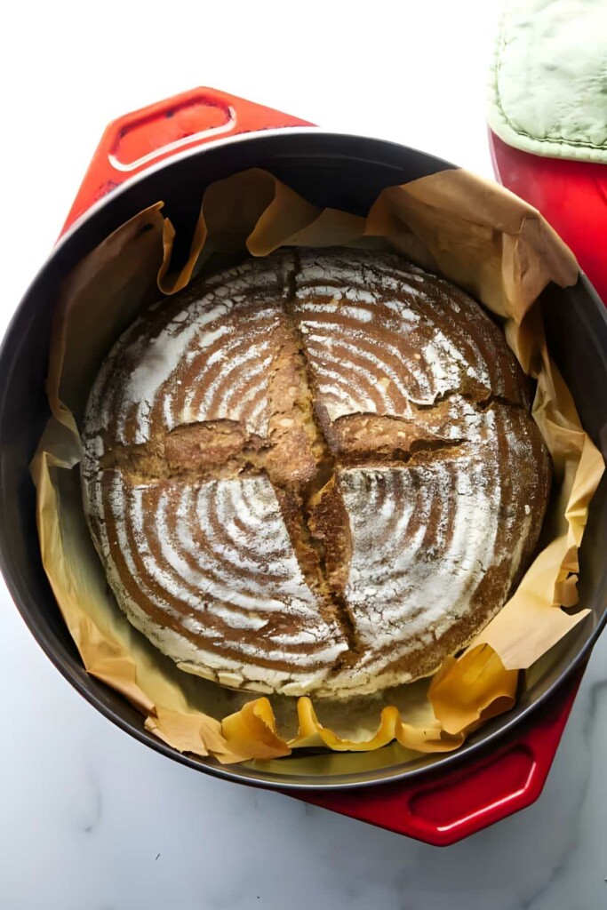 Round artisan spelt bread in red Dutch oven.