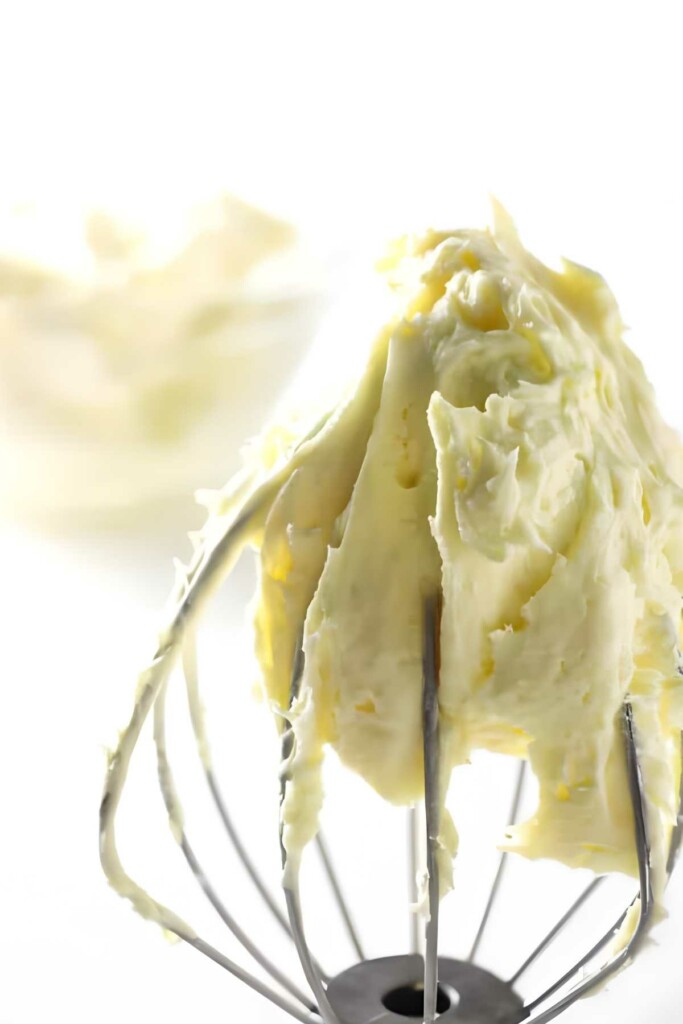 Whisk coated in fluffy vanilla cake filling and a bowl in the background.
