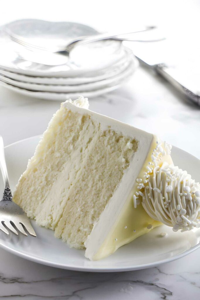 Slice of white chocolate layer cake with sprinkles on plate, fork beside.