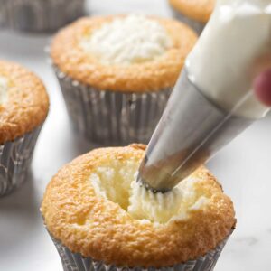 Hand piping white chocolate mousse into a cupcake.