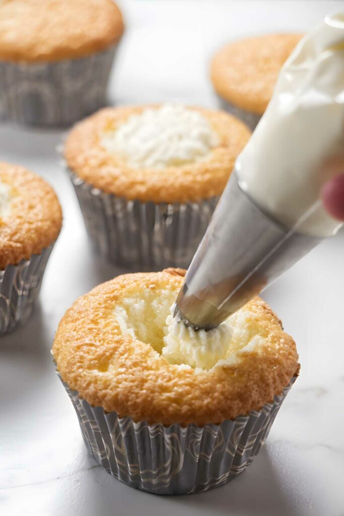 Hand piping white chocolate mousse into a cupcake.