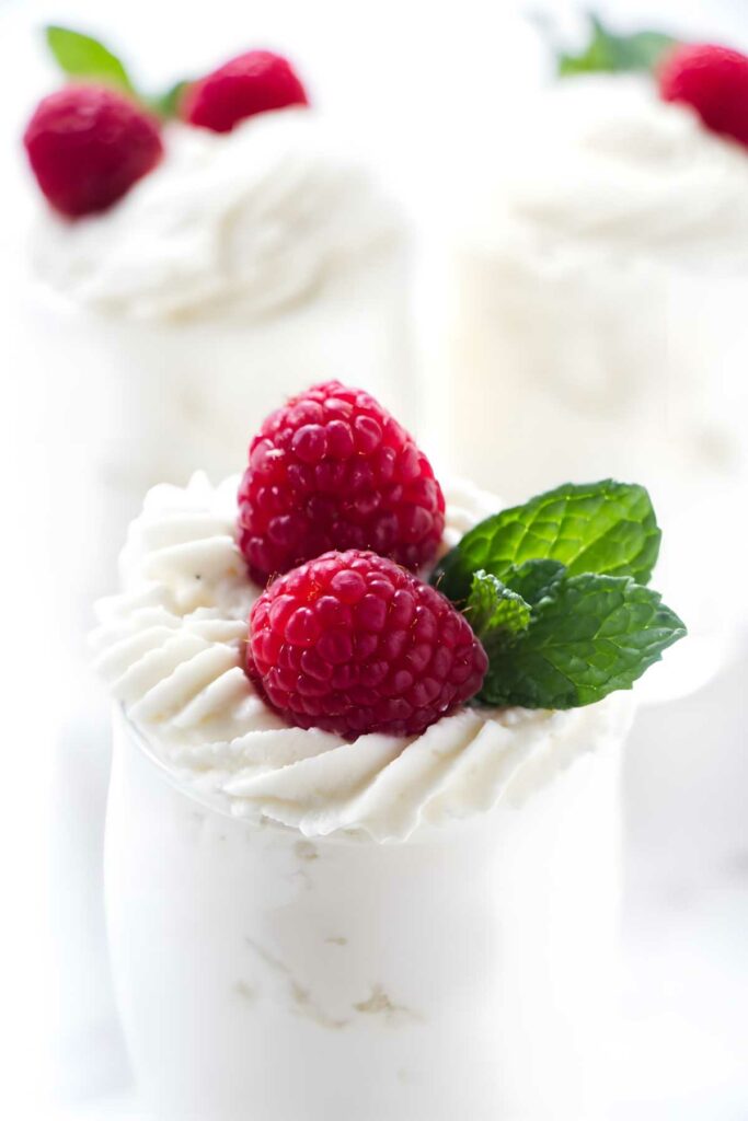 A dessert cup filled with white chocolate mousse, topped with raspberries.