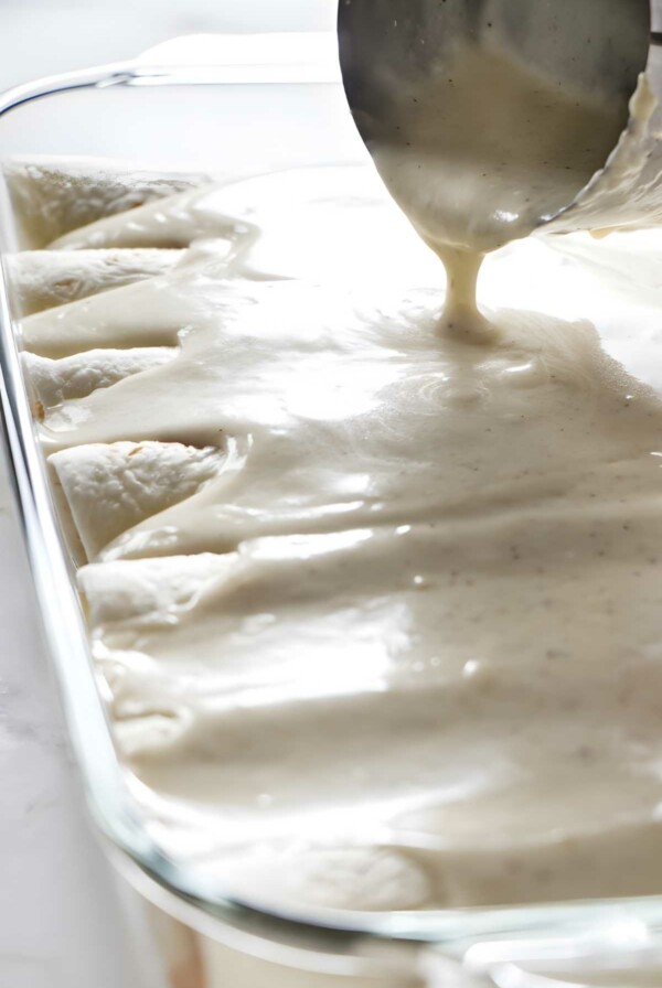 Creamy white sauce poured over enchiladas in a glass baking dish.