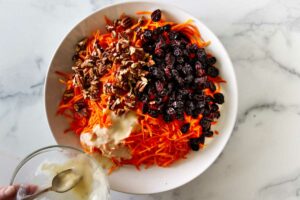 Adding a coleslaw dressing to a grated carrot salad.