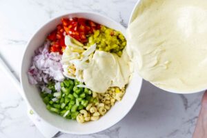 Pouring dressing over a macaroni pasta salad.