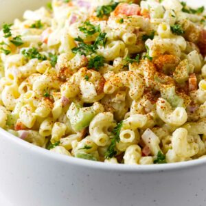 A large bowl filled with macaroni pasta salad topped with paprika.