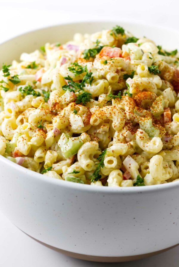 A large bowl filled with macaroni pasta salad topped with paprika.