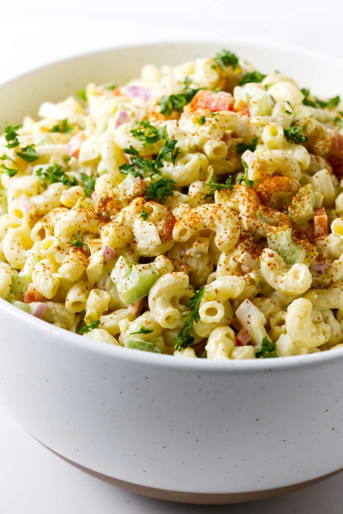A large bowl filled with macaroni pasta salad topped with paprika.