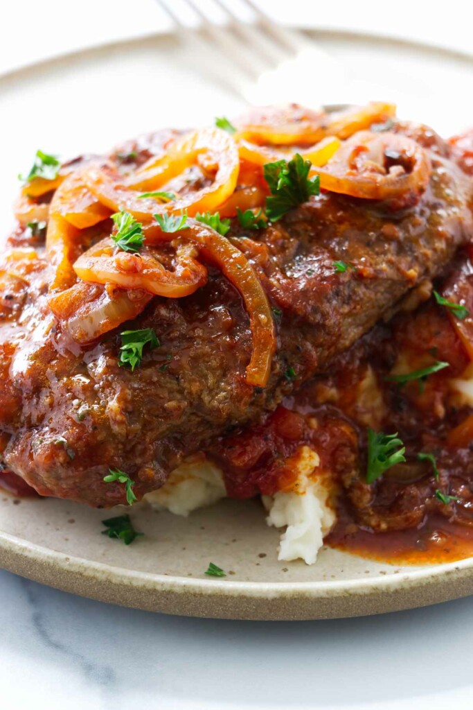 Swiss steak on a pile of mashed potatoes and topped with a tomato sauce.