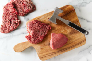 Tenderizing beef round with a meat mallot.