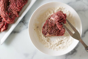 Coating steak in flour to make Swiss steak.