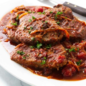 A platter filled with swiss steak with tomato sauce.