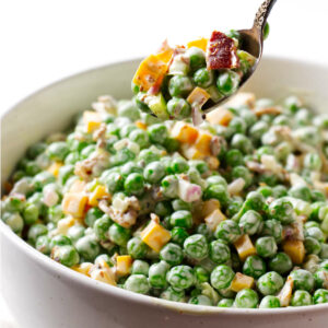 A spoon lifting a serving of cold salad with peas.