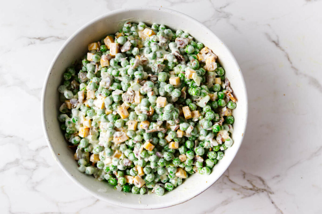 A bowl filled with pea salad made from frozen peas, cheese and bacon.