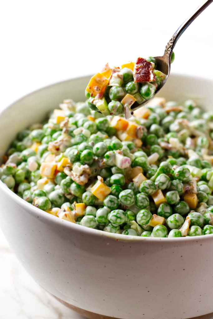 A spoon lifting a serving of pea and cheese salad.