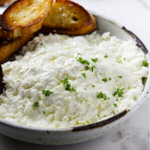 Homemade ricotta cheese in a bowl with toasted bread.