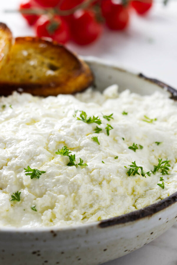 A bowl filled with homemade ricotta cheese next to cherry tomatoes.