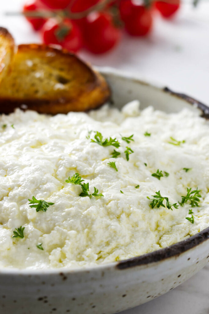 A bowl filled with homemade ricotta cheese next to cherry tomatoes.