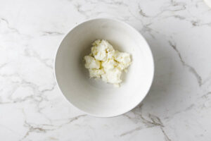 Adding ricotta cheese to a mixing bowl.