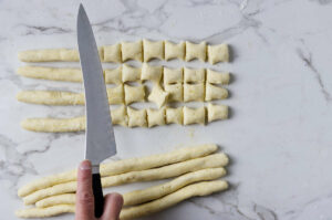 Hand cuts ricotta gnocchi dough into pieces on countertop.