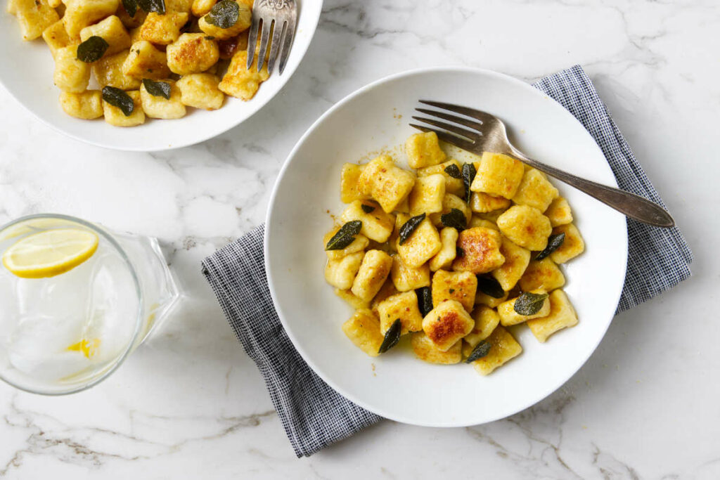 Fluffy gnocchi tossed in sage brown butter sauce in a white pasta bowl.