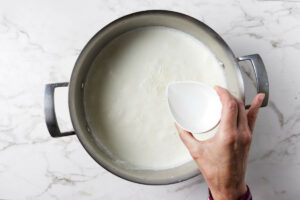 Adding vinegar to hot milk in a pot.
