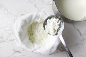 Scooping curds out of the pot and placing them in a strainer.