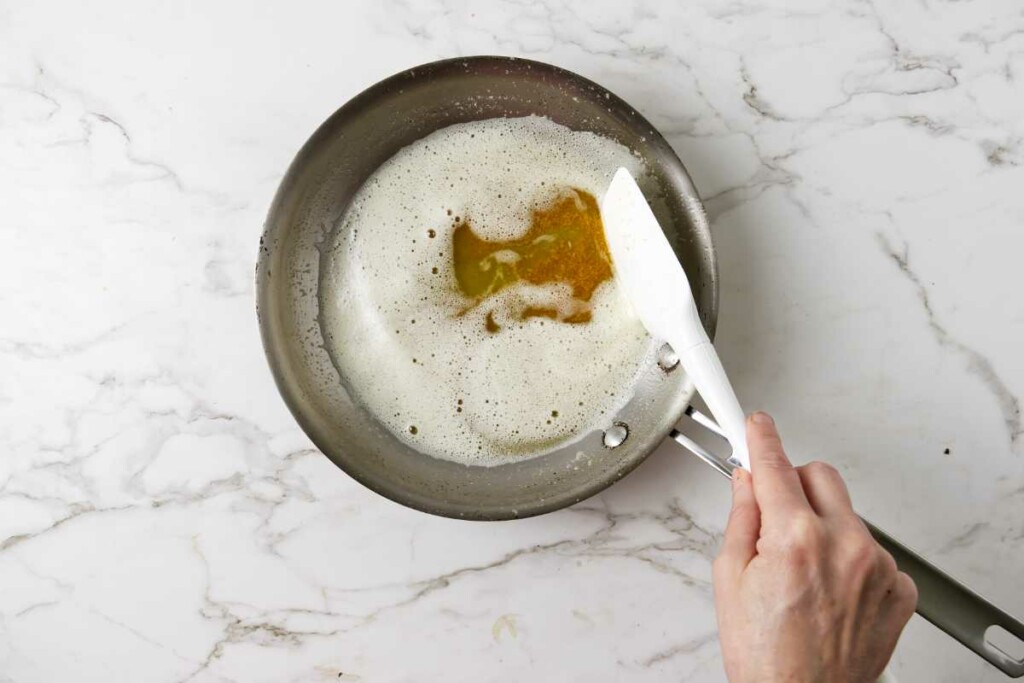 A spatula pushing foam aside from the top of golden brown butter.