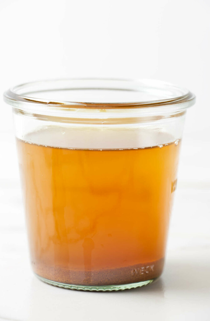 A glass jar with melted golden butter and brown butter solids on the bottom.