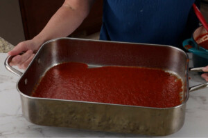 Spreading pasta sauce in the bottom of a baking pan.