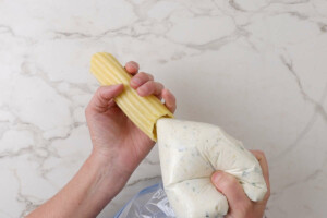 Adding the basil ricotta filling to a manicotti pasta tube.