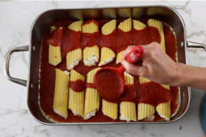 Pouring the marinara sauce over the homemade stuffed pasta dinner.