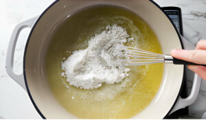Whisking flour into a saucepan with melted butter.
