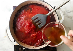 Adding broth to the sauce for beef pasta.
