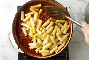 Adding pasta to the sauce in the skillet.