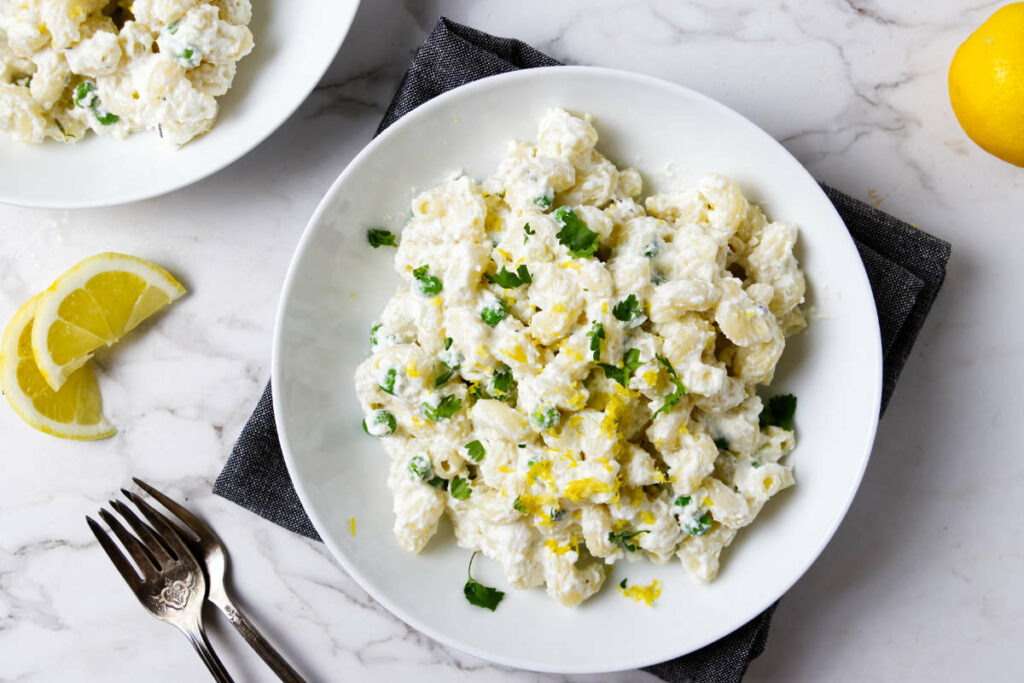 A dinner plate filled with pasta with ricotta and lemon.