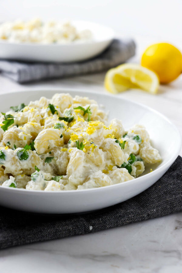 A bowl of lemon and ricotta pasta with fresh lemon in the background.