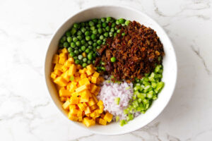 combining all the ingredients for a recipe for green pea salad.